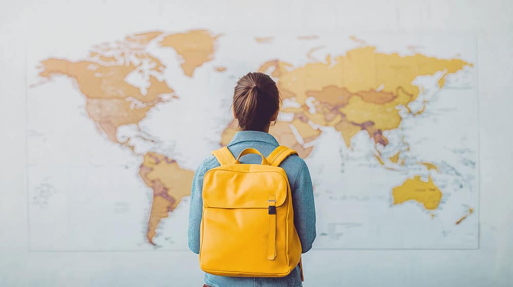 woman with yellow backpack studying world map