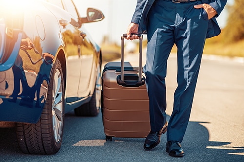 man with luggage walking by rental car
